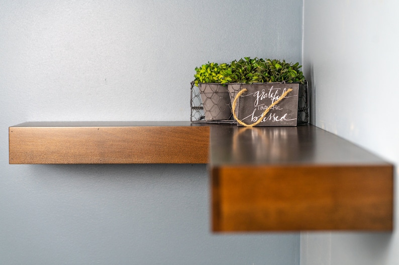 Op de afbeelding: Een houten plank met een draadmand waarin twee kleine potplanten staan. De mand heeft ook een klein bord met de tekst "Grateful, Thankful, Blessed".