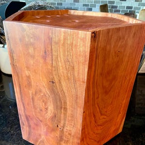 Op de afbeelding: Een zeshoekige houten afvalbak van roodbruin hout met zichtbare nerfpatronen en een natuurlijke afwerking. De deksel is verzonken. Het ontwerp is modern. Geschikt voor keuken of kantoor.