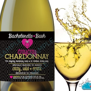 Op de afbeelding: Een fles "Craycray Chardonnay" wijn met een etiket "Bachelorette Bash". Het etiket heeft een ruitpatroon, een roze hart met een ring en tekst die de effecten van de wijn beschrijft. Een glas wijn wordt getoond met een spat.
