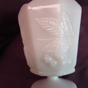 May include: White milk glass pedestal bowl with an embossed design of leaves and berries. The bowl has a scalloped rim and a pedestal base.