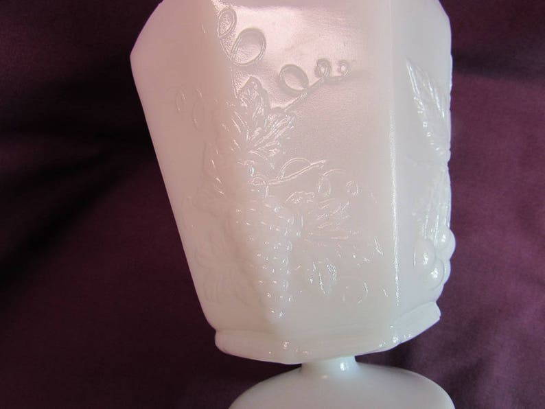May include: White milk glass pedestal bowl with an embossed grapevine design. The bowl has a square base and a round top.