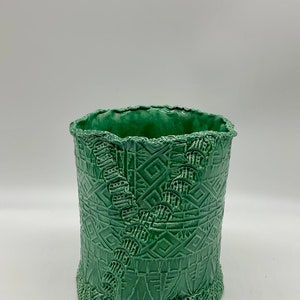 May include: A green ceramic planter with a textured, geometric design. The planter has a scalloped rim and a slightly rounded base.