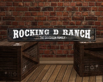 May include: A black wooden sign with white lettering that reads "Rocking D Ranch The Davidson Family". The sign is sitting on top of two wooden crates.