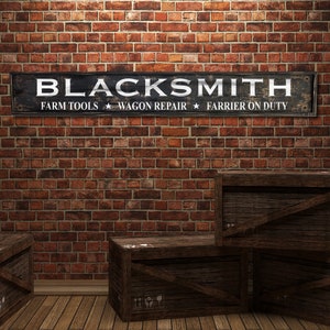 May include: Blacksmith sign with white text on a black background. The sign reads "Blacksmith", "Farm Tools", "Wagon Repair", and "Farrier on Duty". The sign is hanging on a brick wall. There are three wooden crates stacked in front of the sign.