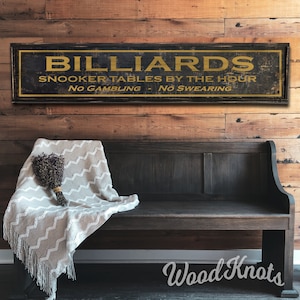 May include: A rustic wooden sign with the text "BILLIARDS" in gold lettering. The sign also reads "Snooker Tables By The Hour" and "No Gambling - No Swearing".
