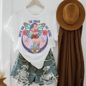 Puede incluir: Camiseta blanca con un gr&aacute;fico de una mujer con alas y el texto "You've had the power all along".
