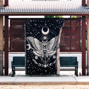 May include: Black tapestry with a white moth design and geometric patterns. The tapestry features a large moth with intricate wings and a celestial theme.