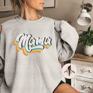 Pode incluir: Camisola cinzenta com um gr&aacute;fico de estilo retro que diz "Mama" em letras coloridas e sobrepostas.