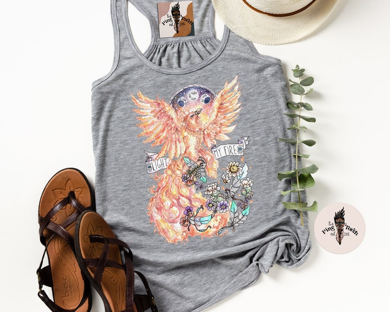 May include: Gray tank top with a phoenix illustration in shades of orange, yellow, and red. The phoenix is surrounded by flowers and the text "My Fire, My Light".