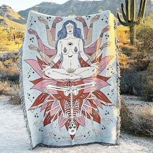 May include: A tapestry featuring a multi-armed goddess figure sitting in a lotus position with a skeleton underneath. The goddess has a third eye and is surrounded by stars. The tapestry is a light blue color with pink and orange accents.