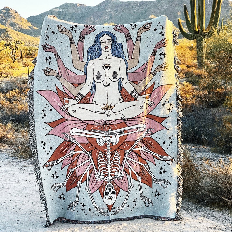 May include: A tapestry featuring a multi-armed goddess figure sitting in a lotus position with a skeleton underneath. The goddess has a third eye and is surrounded by stars. The tapestry is a light blue color with pink and orange accents.