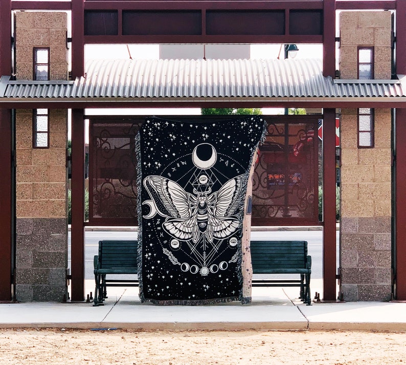 May include: Black tapestry with a white moth design and geometric patterns. The tapestry features a large moth with intricate wings and a celestial theme.
