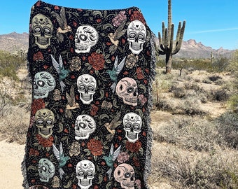 May include: Black throw blanket with a repeating pattern of sugar skulls and floral designs. The skulls are stylized and have a whimsical feel. The blanket is made of a soft, plush fabric.