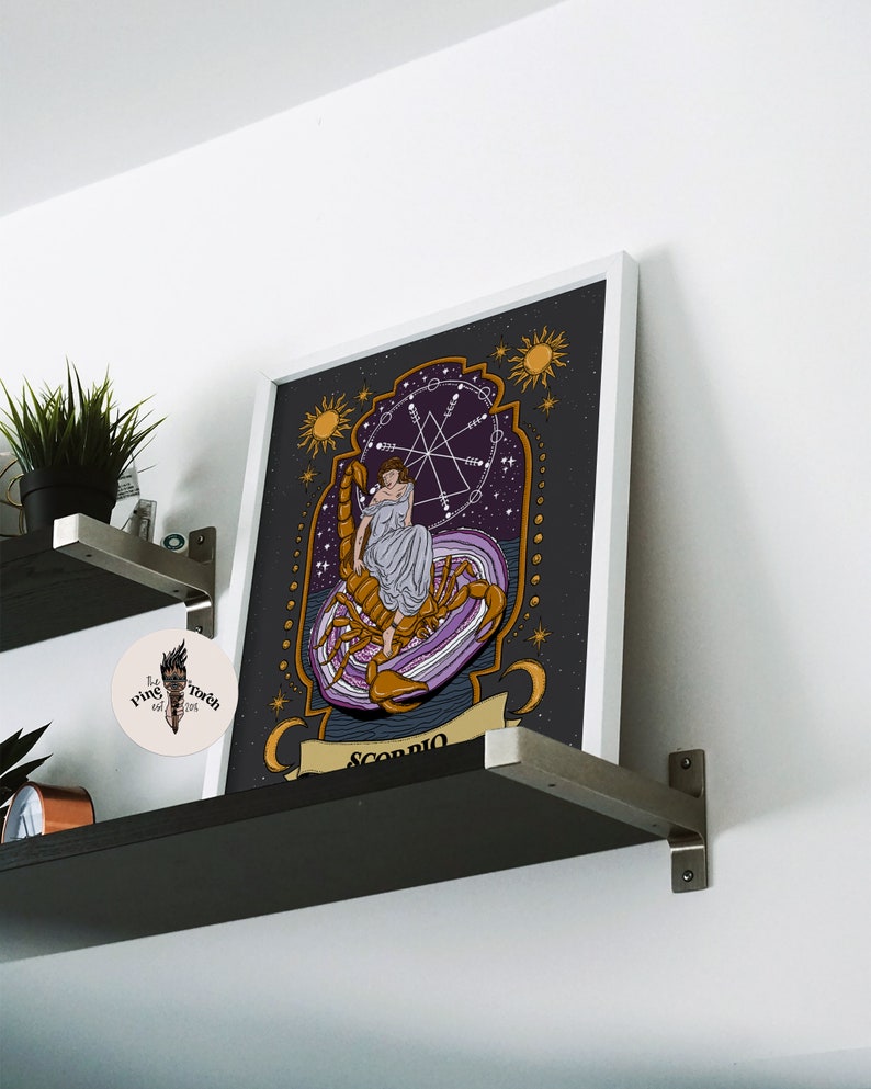 May include: A framed print of a tarot card depicting the Scorpio zodiac sign. The card features a woman sitting on a scorpion with a purple and gold background. The text "Scorpio" is written at the bottom of the card.