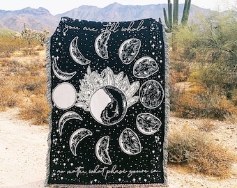 May include: Black and white woven tapestry with a moon phases design and the text "you are still whole no matter what phase you're in".