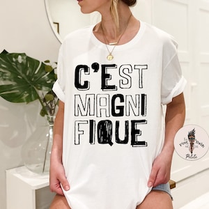 May include: White t-shirt with black text that reads "C'est Magnifique".