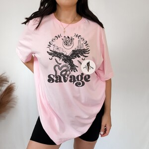 May include: Pink oversized t-shirt with a black and white graphic design featuring a raven, snake, and cactus with the text "Savage".