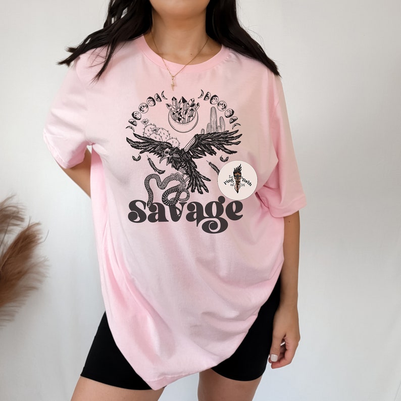 May include: Pink oversized t-shirt with a black and white graphic design featuring a raven, snake, and cactus with the text "Savage".