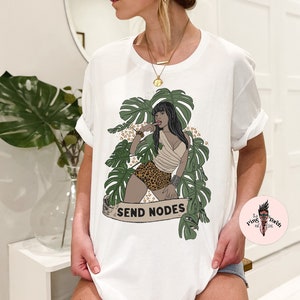 K&ouml;nnte beinhalten: Wei&szlig;es T-Shirt mit einem Aufdruck einer Frau in einer Dschungelkulisse. Die Frau tr&auml;gt einen Bikini mit Leopardenmuster und hat ein tropisches Blatt im Haar. Der Text "SEND NODES" ist auf dem Shirt aufgedruckt.