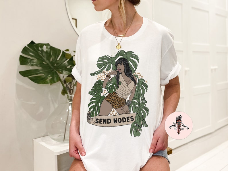 K&ouml;nnte beinhalten: Wei&szlig;es T-Shirt mit einem Aufdruck einer Frau in einer Dschungelkulisse. Die Frau tr&auml;gt einen Bikini mit Leopardenmuster und hat ein tropisches Blatt im Haar. Der Text "SEND NODES" ist auf dem Shirt aufgedruckt.