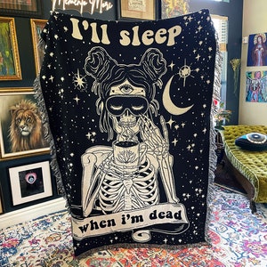 May include: Black throw blanket with a white skeleton illustration holding a coffee cup. The skeleton is wearing a sleep mask and has a third eye. The text on the blanket reads "I'll sleep when I'm dead."
