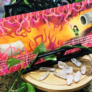 May include: A colorful bookmark with a girl holding a glowing orb in a fiery landscape. The bookmark features the text "For no matter il and damp and quiet your It is eternal and belongs only to you as fiercely, be unar And once you tumel through even the mett remote nestes of your sea Ir the flame that blares for othert, at the noen plout, unsched Do not fear for even the war cavernous Ce has a path ta he have latt their way"