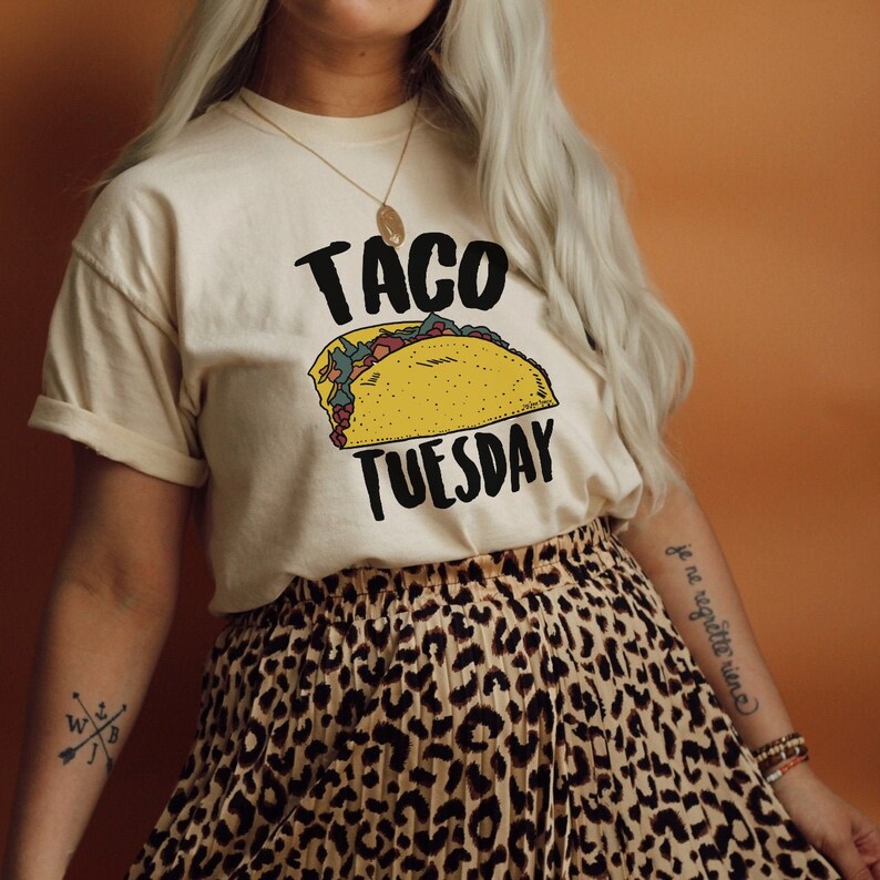 May include: A white t-shirt with the text "Taco Tuesday" and a cartoon image of a taco. The person wearing the shirt is also wearing a leopard print skirt.