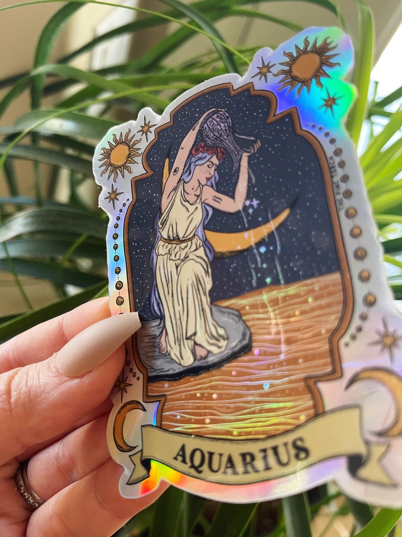 以下が含まれることがあります： ホログラフィックステッカー、水瓶座の星座デザイン。イラストは、三日月のある星空を背景に、女性が容器から水を注いでいる様子を描いています。「AQUARIUS」の文字がバナーに表示されています。