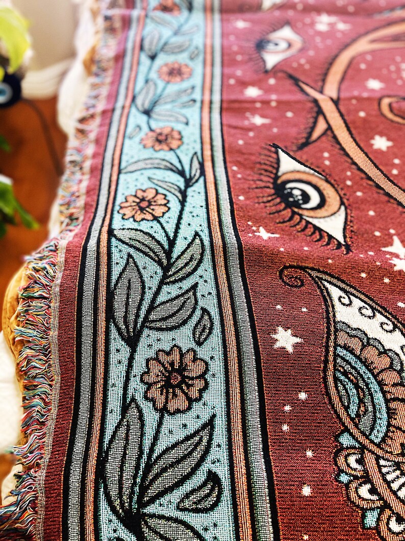 May include: A red woven tapestry with a floral border and a paisley design. The tapestry features a repeating pattern of eyes with eyelashes and stars.