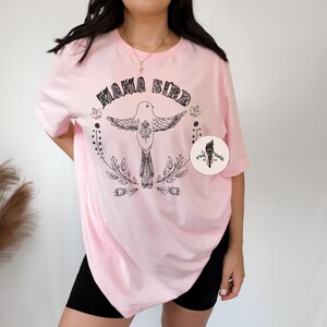 May include: Pink oversized t-shirt with a black graphic of a bird with the text "Mama Bird" and a small logo in the bottom right corner.