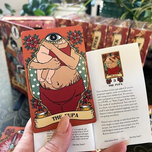 May include: A red and green illustrated card with a woman holding a baby. The card is from the "The Mom Deck" and is titled "The FUPA". The card number is 3.