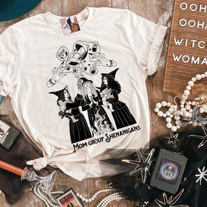 K&ouml;nnte beinhalten: Ein wei&szlig;es T-Shirt mit einer schwarz-wei&szlig;en Illustration von drei Hexen mit dem Text "Mom Group Shenanigans".