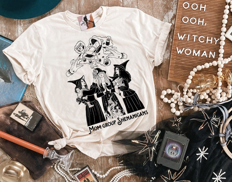 K&ouml;nnte beinhalten: Ein wei&szlig;es T-Shirt mit einer schwarz-wei&szlig;en Illustration von drei Hexen mit dem Text "Mom Group Shenanigans".