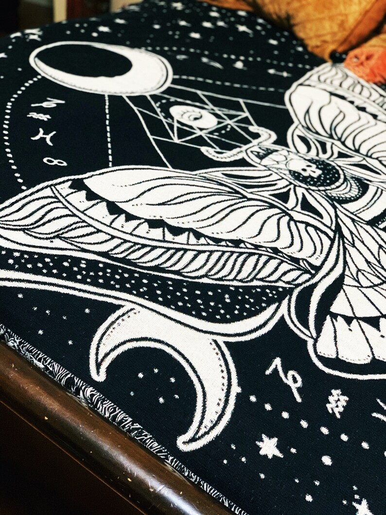May include: Black and white tapestry featuring a moth with intricate wings and a crescent moon design. The tapestry has a starry background and the text "19" in the bottom right corner.