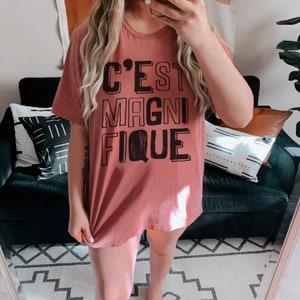 May include: A mauve t-shirt with the text "C'EST MAGNIFIQUE" printed in black.