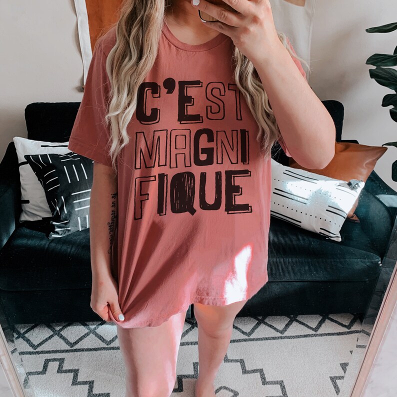 May include: A mauve t-shirt with the text "C'EST MAGNIFIQUE" printed in black.