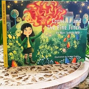 May include: A children's book cover with a green background and a girl holding a flaming torch. The title is "Cornelia and The Pine Torch" by Mari Toscas, MFA. The illustrations are by luciana Guerra.