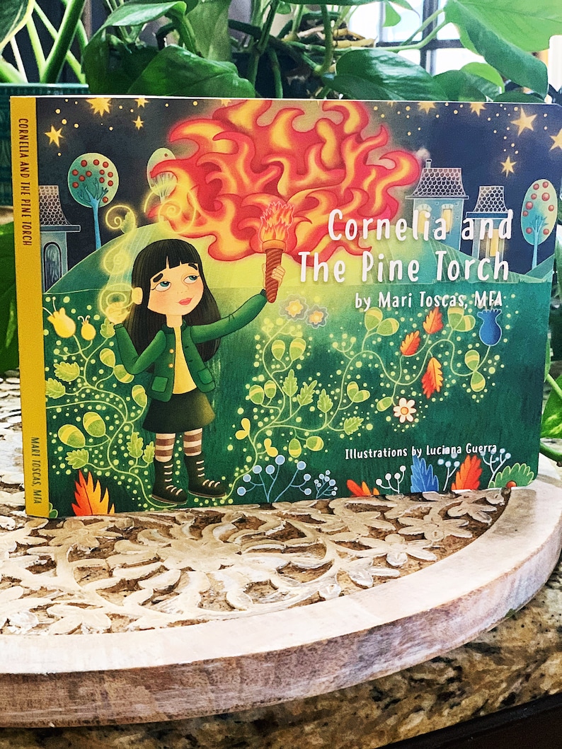 May include: A children's book cover with a green background and a girl holding a flaming torch. The title is "Cornelia and The Pine Torch" by Mari Toscas, MFA. The illustrations are by luciana Guerra.