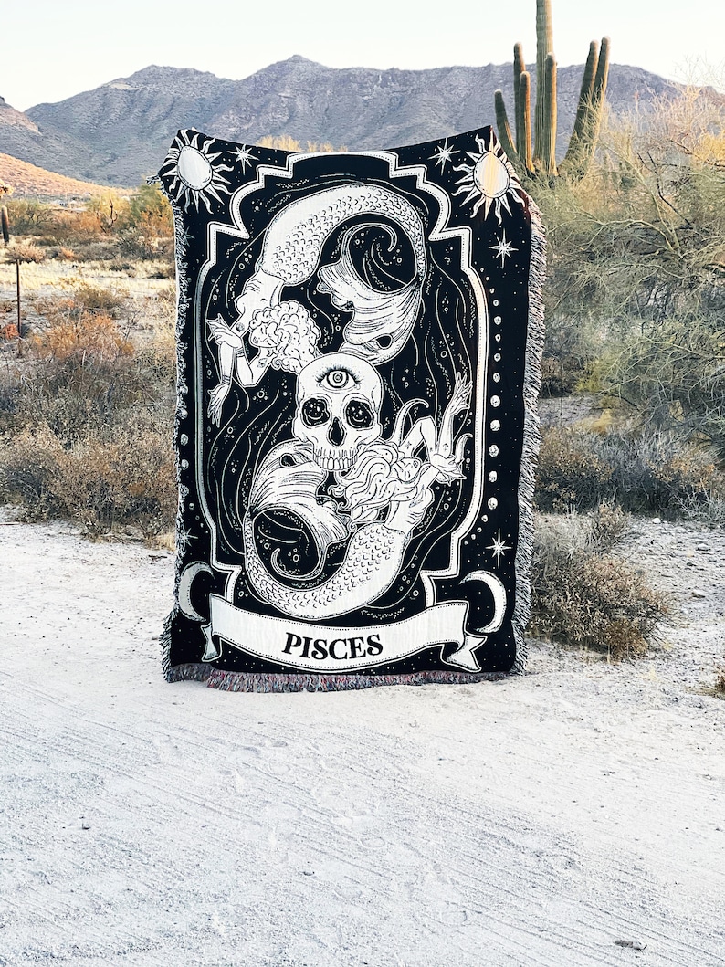 Op de afbeelding: Zwart-witte wandkleed met een zeemeermin, schedel en sterren. Het wandkleed heeft de tekst "Pisces" erop.