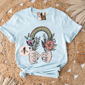 May include: Light blue t-shirt with a rainbow, flowers, and two fists with the words "Girl Power" and "The Pink Torch".