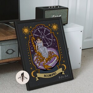 May include: A black framed print of a zodiac sign, Scorpio, with a woman sitting on a scorpion. The print has a purple and gold color scheme and features a celestial design with stars and moons. The text "The Pine Tree" is at the bottom of the print.
