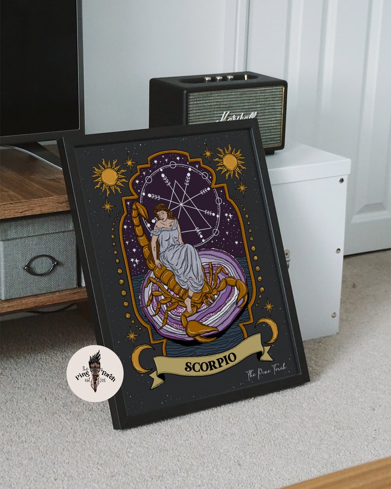 May include: A black framed print of a zodiac sign, Scorpio, with a woman sitting on a scorpion. The print has a purple and gold color scheme and features a celestial design with stars and moons. The text "The Pine Tree" is at the bottom of the print.