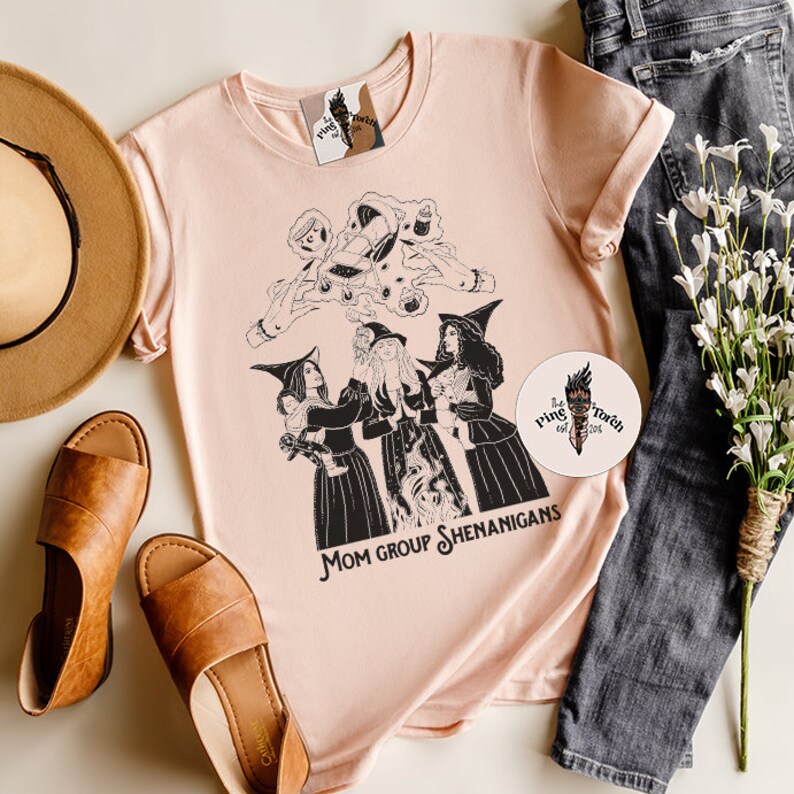 K&ouml;nnte beinhalten: Ein pinkfarbenes T-Shirt mit einer schwarz-wei&szlig;en Illustration von drei Hexen mit dem Text "Mom Group Shenanigans".