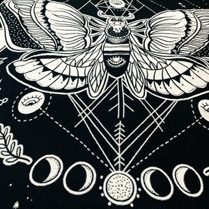 May include: Black and white tapestry featuring a moth with intricate wings and a geometric design. The moth is surrounded by moons and stars.