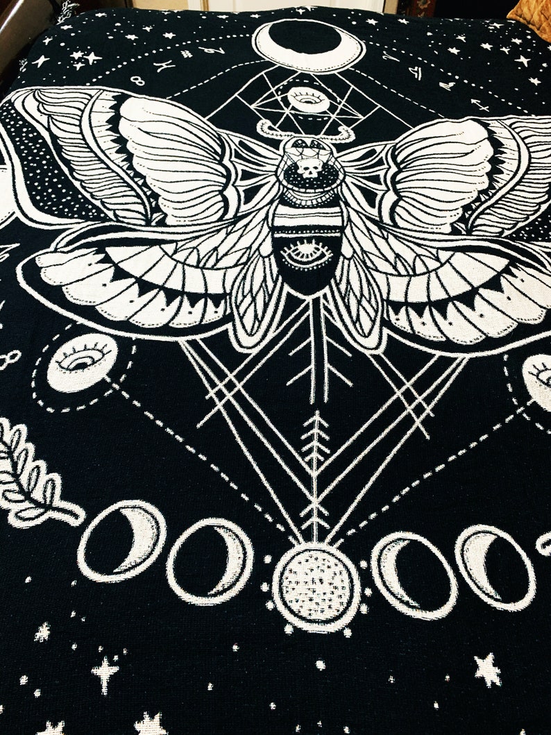 May include: Black and white tapestry featuring a moth with intricate wings and a geometric design. The moth is surrounded by moons and stars.