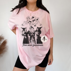 K&ouml;nnte beinhalten: Pinkes T-Shirt mit einer schwarz-wei&szlig;en Illustration von drei Hexen mit dem Text "Mom Group Shenanigans".