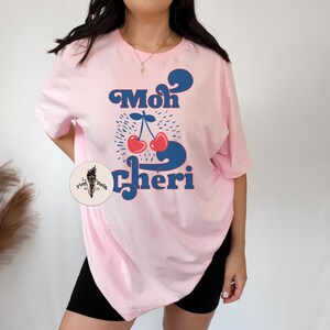 May include: Pink t-shirt with a blue and red graphic of cherries and the text "Mon Cheri" in a retro font.