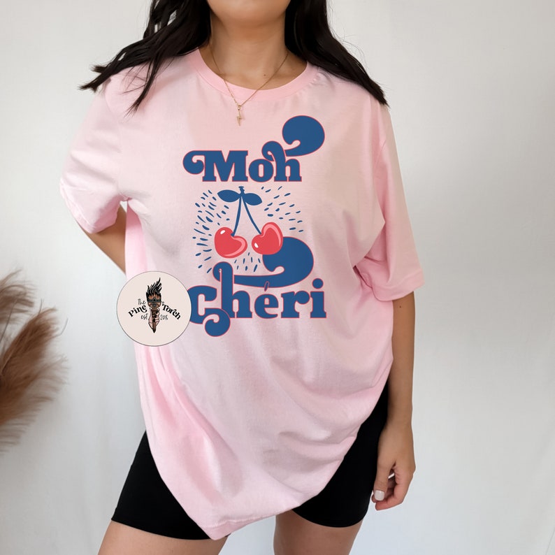 May include: Pink t-shirt with a blue and red graphic of cherries and the text "Mon Cheri" in a retro font.