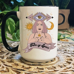 May include: White ceramic mug with a black handle. The mug features a colorful illustration of a woman with pink hair, a third eye, and a lotus flower. The text "Take up Space" is written in a retro font on a banner.