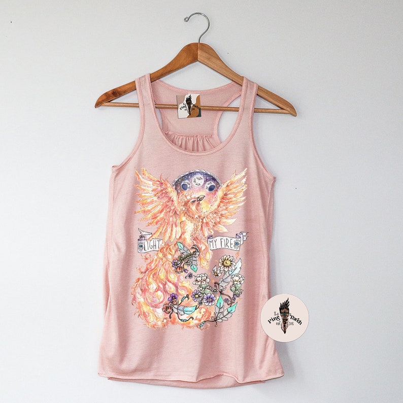 May include: A pink tank top with a graphic of a phoenix with the text "Light My Fire" printed on it. The phoenix is surrounded by flowers and fire.